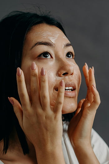 Asian woman, applying moisturizer, healthy skin, studio setting, touching face, looking up, skincare routine, beauty treatment, facial care, natural beauty, skincare products