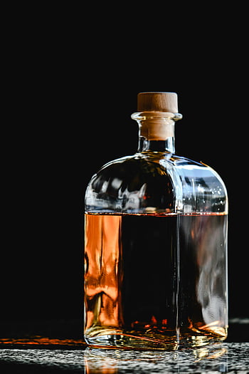 clear glass bottle, brown liquid, whiskey bottle, cork stopper, black backdrop, stylish glass, dramatic background, amber liquid, transparent bottle, alcohol bottle, dark background