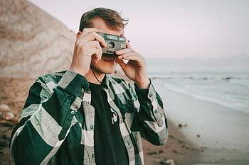 analog camera, beach photography, coastal views, young man, taking picture, scenic views, outdoor photography, analog photography, beach scene, casual attire, flannel shirt