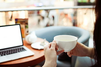žena držící šálek, Moderní kavárna, macbook pro, bílý keramický šálek, uvolněná scéna, laptop na stole, Vnitřní nastavení, neformální atmosféra, Ambiance kavárny, Práce v kavárně, útulné prostředí