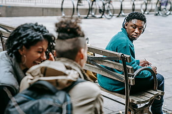 students gossiping, laughing, black man, diverse group, young adults, street bench, conversation, outdoor setting, casual interaction, urban scene, headphones