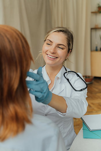 Tenaga kesehatan, Kemeja lengan panjang putih, wanita yang tersenyum, Pemeriksaan pasien, Pengaturan dalam ruangan, perawatan kesehatan yang positif, sarung tangan medis, stetoskop, Dokter yang ceria, Pengalaman perawatan kesehatan, perawatan pasien