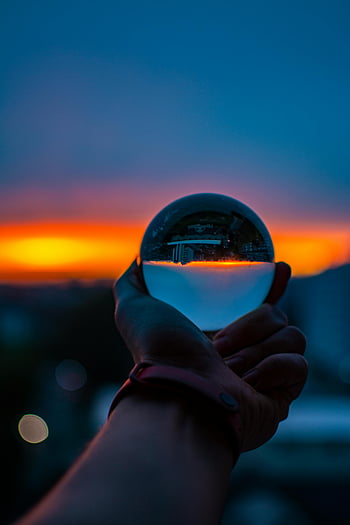 Mano de sujeción de vidrio, reflejo del horizonte del atardecer, colores vibrantes, bola de cristal, Mano de primer plano, colores del atardecer, Reflexión del paisaje urbano, orbe de cristal, fotografía de mano, fotografía de atardecer, vidrio reflectante