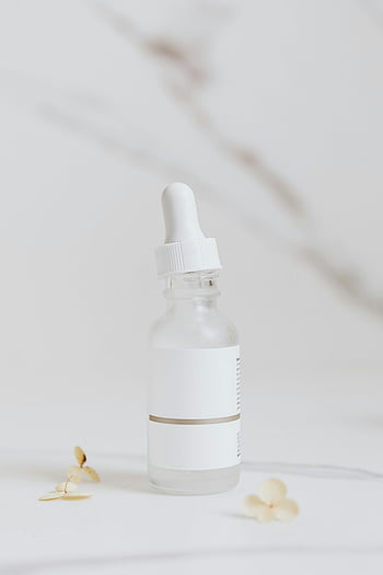 white serum bottle, white surface, elegant product photography, glass serum bottle, white flowers, minimalistic design, skincare product, clean aesthetic, beauty product, white background, product photography