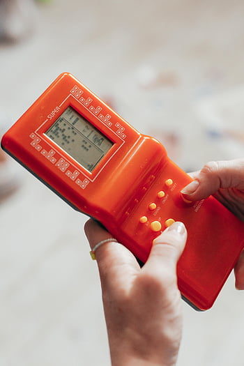 retro handheld gameconsole, close-up fotografie, Handen spelen, nostalgie, vintage gaming, retro gaming, handheld console, Close-up shot, gaming nostalgie, Orange Game Console, retro gamepad