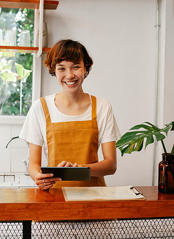 Dipendente allegro, tavoletta, bancone del caffè, barista, Café affascinante, pianta, appunti, grembiule, sorridente, contatore di legno, impostazione interna