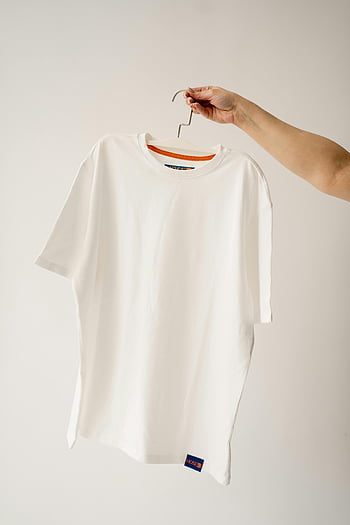 white t-shirt, hanger, human hand, studio background, clean t-shirt, white background, clothing display, t-shirt on hanger, minimalist photography, fashion photography, product photography