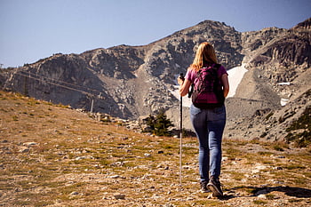 woman hiking, scenic mountain trail, clear daylight, embracing adventure, outdoor adventure, mountain landscape, hiking pole, backpack, nature exploration, scenic view, daylight hike
