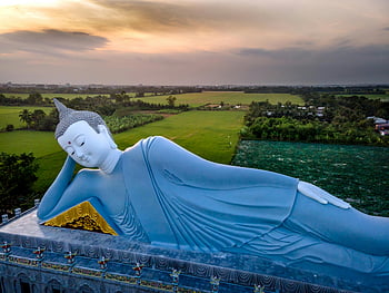 Sleeping Buddha, green field, aerial view, serene statue, lush fields, sunset, reclining Buddha, stunning view, peaceful landscape, Buddha statue, countryside scenery