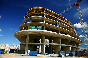unfinished gray concrete building, circular building, under construction, crane, clear blue sky, low angle view, construction site, building construction, concrete structure, blue sky, construction crane