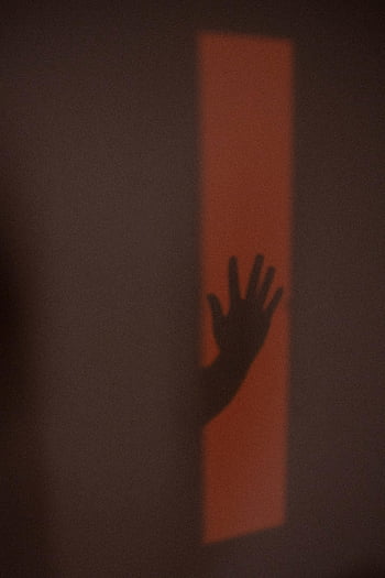 handschaduw, anonieme persoon, sinaasappelmuur, mysterieuze atmosfeer, rustige stemming, schaduwfotografie, menselijke hand, muurschaduw, licht en schaduw, artistieke schaduw, minimalistische fotografie
