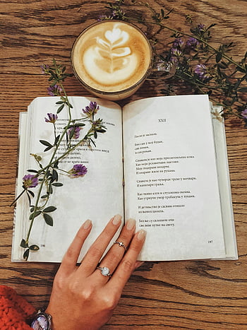 latte, open book, wooden table, flowers, poetry, beverage in cup, relaxing scene, coffee art, reading moment, hand with rings, cozy atmosphere