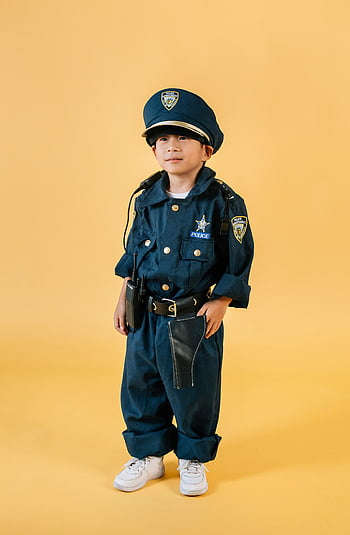 child, policeman costume, studio photo, yellow backdrop, police officer, young child, confident pose, ambition, dreams, cosplay, Halloween costume