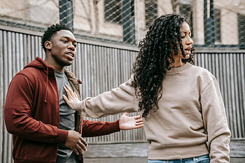 Mann und Frau streiten sich, Paar Meinungsverschiedenheiten, Legere Kleidung, draußen, grauer Zaunhintergrund, emotionale Szene, städtischen Umfeld, Handbewegungen, intensives Gespräch, Beziehungskonflikt, öffentliches Argument