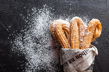 churros, powdered sugar, freshly baked, dessert treat, close-up, newspaper, tasty, sweet snack, fried pastry, sugar dusting, dark background