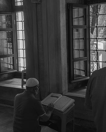 L'uomo che legge il Corano, vista posteriore, grande finestra, Greyscale Indoor, ambientazione religiosa, Preghiera islamica, Studio del Corano, interno della moschea, lettura spirituale, Adorazione musulmana, contemplazione tranquilla