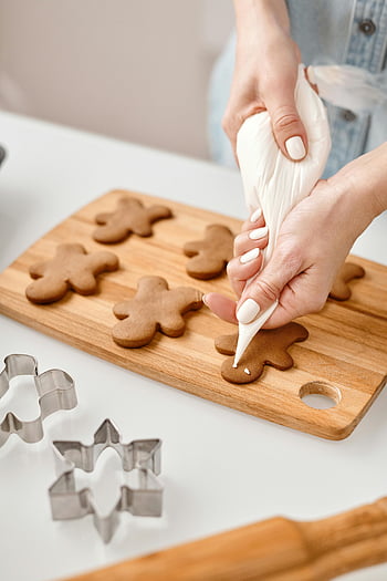 gingerbread man cookies, decorating gingerbread cookies, icing, festive preparation, hands, cookie cutters, wooden cutting board, holiday baking, gingerbread men, festive cookies, cookie decoration
