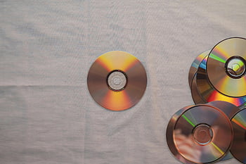 Compact Discs, white textile, colorful reflections, aesthetic top view, multiple CDs, plain surface, disc collection, music storage, reflective surface, flat lay, minimalist design