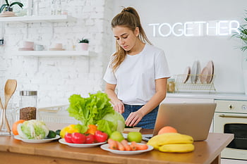 woman preparing vegetables, bright kitchen, white t-shirt, fresh vegetables, laptop, kitchen counter, healthy eating, cooking, woman in kitchen, together sign, kitchen scene