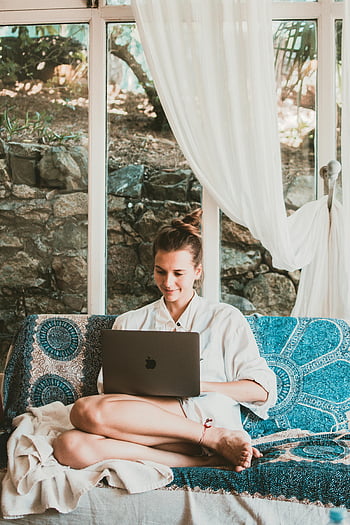 χαμογελαστή γυναίκα, Χρήση MacBook, κάθονται στον καναπέ, Ρύθμιση απομακρυσμένης εργασίας, άνετος καναπές, γαλήνιο περιβάλλον, χρήστης φορητού υπολογιστή, γραφείο στο σπίτι, Περιστασιακή εργασία, εσωτερική ρύθμιση, φόντο πέτρινο τοίχο