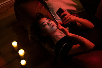 žena relaxující uvnitř, chytrý telefon, světlo svíček, příjemný večer, domácí interiér, intimní, náladový, osobní čas, technologie, teplý, mladého dospělého