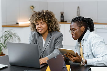 Frau im grauen Blazer, Mann in weißen langen Ärmeln, Laptop, Tablette, modernes Büro, Profis diskutieren, Projektzusammenarbeit, Arbeitsumgebung, Geschäftstreffen, Büroeinstellung, technologische Nutzung
