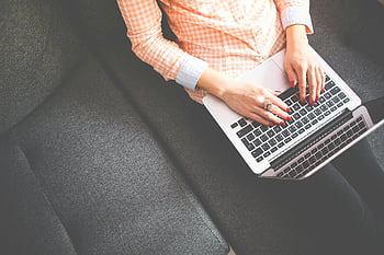 žena psaní, laptop, šedá pohovka, ležérní oblečení, při pohledu shora, macbook, pracování z domova, pohodlné nastavení, vnitřní scéna, uvolněné držení těla, využití technologie