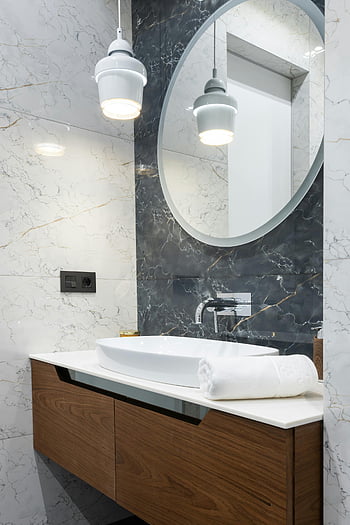 modernes Badezimmer, Marmorwände, runder Spiegel, Holzschrank, stilvolles Badezimmer, Sauberes Badezimmer, sinken, Pendelleuchten, zeitgemäßes Design, Innenarchitektur, weißes Handtuch