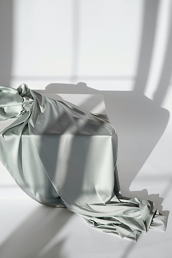 gray textile, white table, silk fabric, draped fabric, intricate shadows, soft natural light, gray silk, table shadows, fabric texture, elegant draping, minimalist composition
