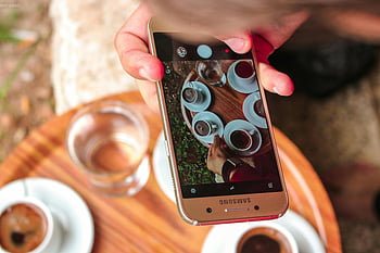 Samsung Galaxy, smartphone, taking picture, coffee cups, wooden table, outdoors, hand holding, photo capturing, coffee scene, outdoor setting, smartphone photography
