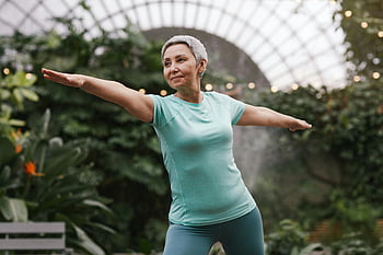 elderly woman, warrior pose, yoga, indoor botanical garden, lush green, fitness, active lifestyle, senior health, exercise, meditation, wellness