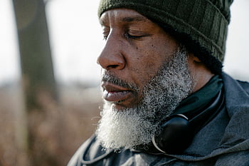 serious bearded black man, warm clothes, closed eyes, close-up profile, meditating outdoors, headphones, peaceful demeanor