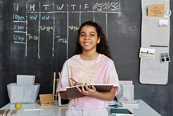 girl in pink shirt, holding notebook, smiling teen girl, classroom, chalkboard timetable, education, student, learning, school, study, desk
