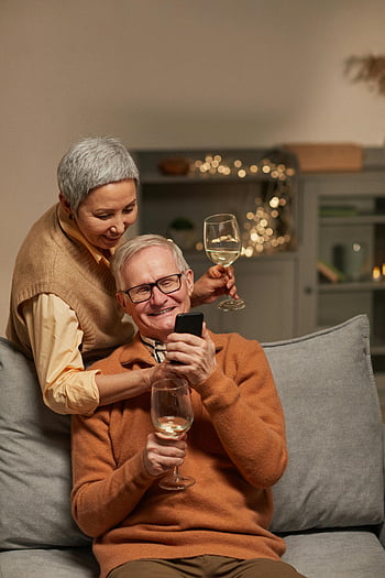 senior couple, smiling, smartphone, wine glasses, leisure time, technology, indoors, cozy setting, happy seniors, enjoying moment, home relaxation