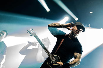 man in black shirt, black electric guitar, live music performance, energetic guitarist, stage performance, bright lights, tattooed musician, rock concert, music festival, stage spotlight, black crew neck shirt