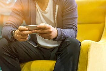 man using smartphone, yellow chair, technology use, mobile phone, sitting man, smartphone user, casual setting, indoor scene, modern technology, relaxed posture, digital device