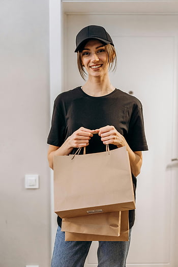 woman, black crew neck t-shirt, brown paper bag, black cap, paper shopping bags, smiling, indoors, casual outfit, delivery person, casual style, everyday look