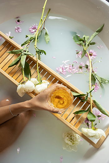 woman taking bath, glass of wine, bathtub with flowers, relaxation, self-care, soothing scene, bath tray, floral bath, bath time, spa-like, tranquil setting