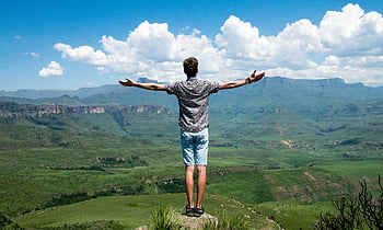 man, grey shirt, elevated surface, mountain view, open arms, scenic landscape, blue sky, clouds, outdoor adventure, nature, travel photography