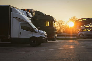 motor vehicles, parked trucks, car transporter, open parking lot, sunset scene, golden hour, row of trucks, vehicle parking, truck parking, car transport, open lot parking