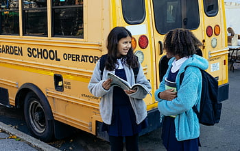cute children, diverse children, school bus, schoolgirls, wearing uniforms, chat happily, yellow school bus, school uniforms, school environment, outdoor scene, school activities