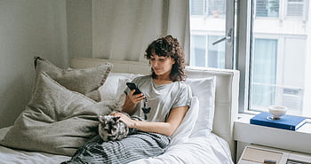 γυναίκα περιηγείται σε smartphone, ζεστή εσωτερική σκηνή, Γυναίκα ξαπλωμένη στο κρεβάτι, Γάτα, γαλήνια σκηνή, smartphone, κρεβάτι, μαξιλάρια, παράθυρο, ζεστή ατμόσφαιρα, Γυναίκα με γάτα