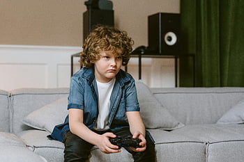 Ragazzo che gioca ai videogiochi, Ragazzo dai capelli ricci, divano comodo, Gaming interno, controller di videogiochi, impostazione del soggiorno, Giochi focalizzati, Abbigliamento da gioco casual, intrattenimento domestico, gioco intenso