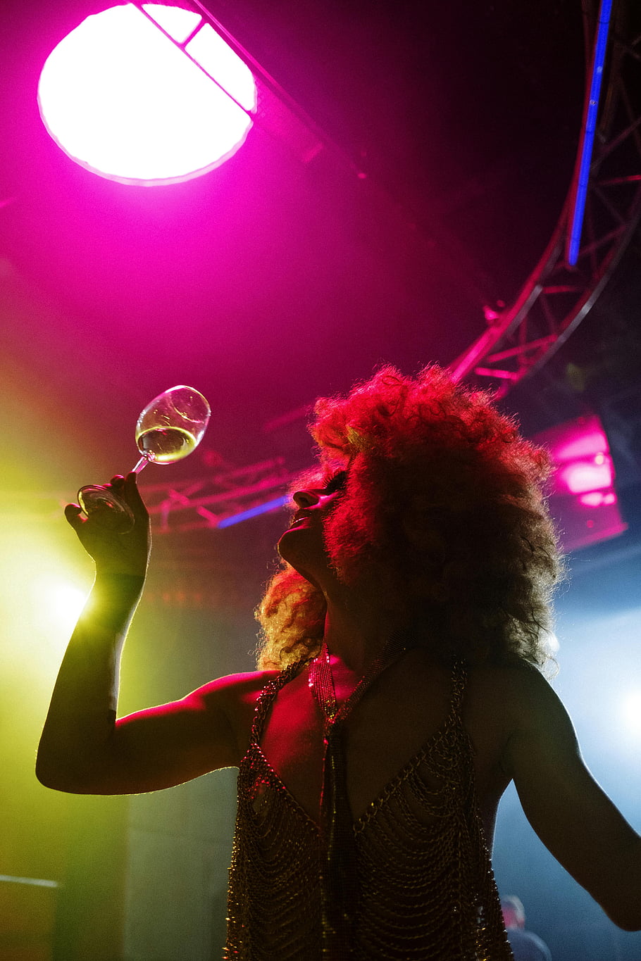 glamorous performer, nightlife, spotlight, drink, silhouette, stage lighting, wine glass, curly hair, sequined dress, vibrant colors, entertainment venue