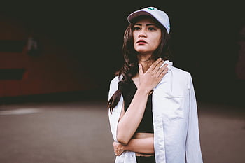 flache Fokusfotografie, selbstbewusste Frau, lässige Streetwear, Porträt im Freien, dunkler Hintergrund, junge Frau, Streetstyle, urbane Mode, weiße Jacke, Deckel, selbstbewusste Pose