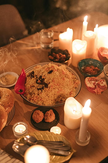 Ramadan meal, traditional dishes, wooden table, burning candles, cooked food, warm setting, inviting atmosphere, pomegranate, rice dish, flatbread, candlelight dinner
