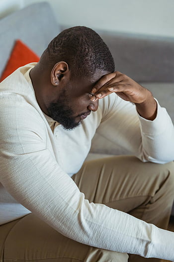 nachdenklich schwarzer Mann, auf dem Sofa sitzen, Kopf gesenkt, Stress, ermüden, Seitenansicht, drinnen, Stress ausdrücken, Müdigkeit ausdrücken, Mann im weißen Hemd, Mann auf Couch