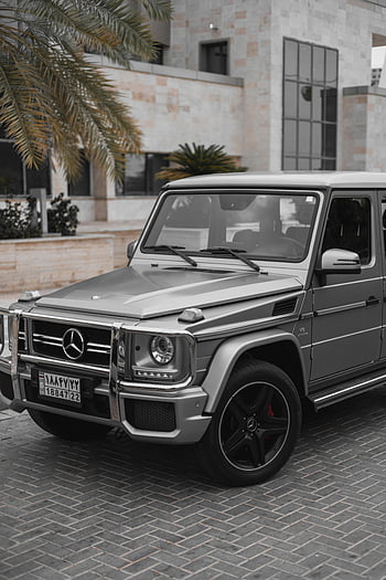 Šedý Mercedes třídy G, Mercedes G-Class SUV, Moderní městské prostředí, stylové šedé SUV, městské parkování, luxusní vozidlo, mercedes-benz, g-třída, šedé auto, moderní architektura, panoráma pozadí