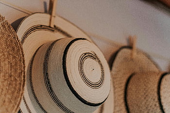 brown straw hat, handmade straw hats, intricate patterns, hanging hats, indoor display, close-up photo, creative design, natural materials, artisanal hats, decorative hats, straw hat patterns