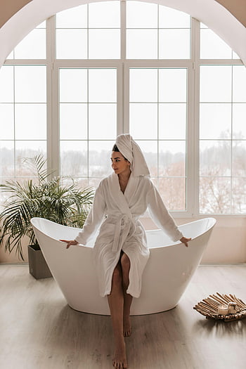 Donna in accappatoio bianco, Seduto sulla vasca da bagno, rilassante in casa, accappatoio e asciugamano, bordo vasca, Rilassamento indoor, grande finestra, bagno moderno, Atmosfera accogliente, impostazione simile a una spa, tranquillità interna